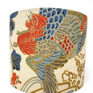 Op de afbeelding: Een crèmekleurige lampenkap met een kleurrijk Japans geïnspireerd ontwerp met een rode, blauwe en gouden vogel met ingewikkelde details. De vogel wordt omringd door bloem- en wolkachtige patronen.