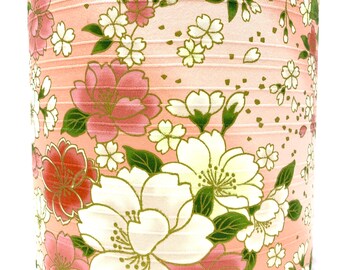 May include: A pink lampshade with a floral pattern featuring white and pink flowers with green leaves. The flowers have gold accents.