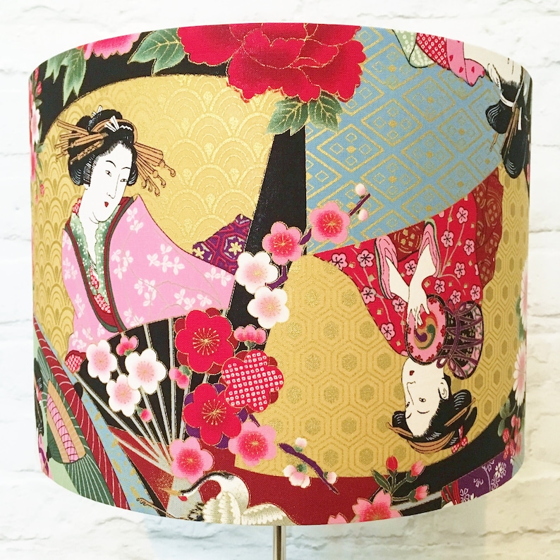 Puede incluir: Una pantalla de l&aacute;mpara con un dise&ntilde;o japon&eacute;s colorido que presenta a dos mujeres con ropa tradicional, flores de cerezo y detalles dorados.