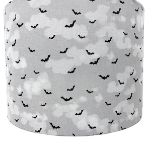 Puede incluir: Una pantalla de lámpara gris con un patrón de murciélagos negros. Los murciélagos vuelan sobre un fondo de nubes blancas.
