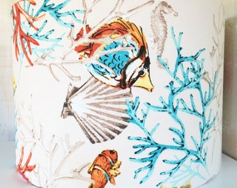 May include: A white lampshade with a colorful sea life design. The design features blue, orange, and brown fish, coral, and seashells.