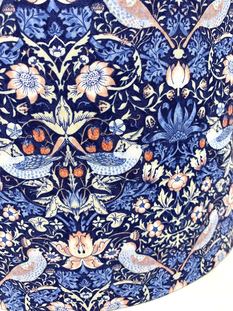 May include: A navy blue fabric with a repeating pattern of stylized birds, flowers, and leaves. The pattern is in shades of blue, pink, and white.