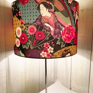 Puede incluir: Una l&aacute;mpara de mesa con una base plateada y una pantalla de tela con una geisha japonesa con un dise&ntilde;o floral en tonos de rosa, rojo, amarillo y verde.