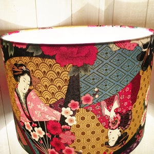 Puede incluir: Una pantalla de l&aacute;mpara con un dise&ntilde;o colorido de inspiraci&oacute;n japonesa que presenta geishas, flores y patrones geom&eacute;tricos. La pantalla de la l&aacute;mpara est&aacute; hecha de tela y tiene una forma redonda.