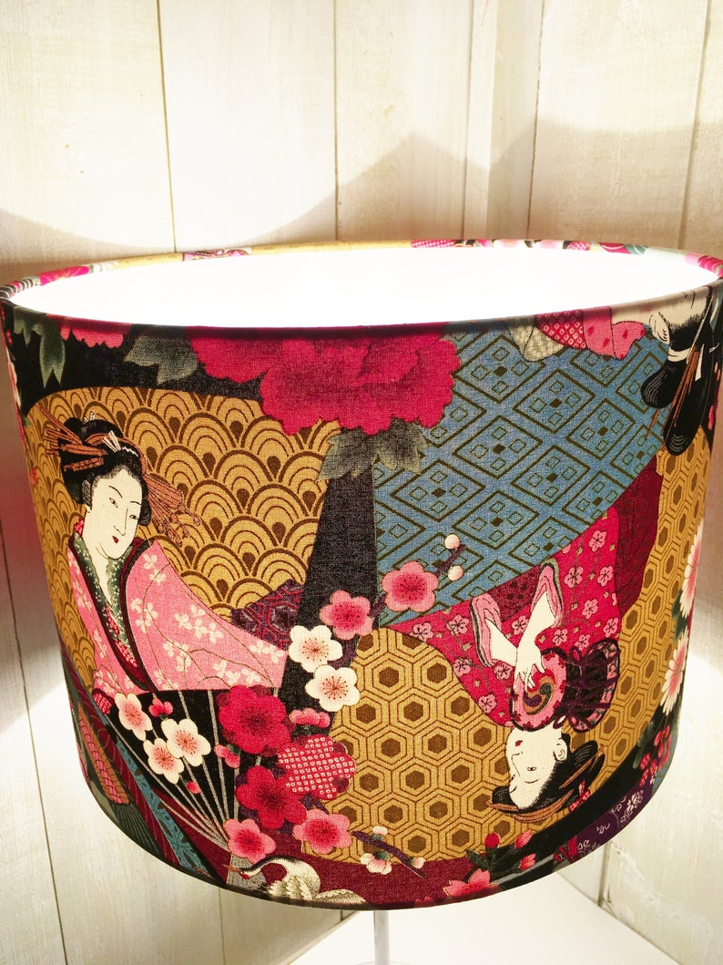 Puede incluir: Una pantalla de l&aacute;mpara con un dise&ntilde;o colorido de inspiraci&oacute;n japonesa que presenta geishas, flores y patrones geom&eacute;tricos. La pantalla de la l&aacute;mpara est&aacute; hecha de tela y tiene una forma redonda.