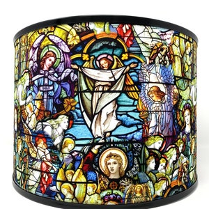 Puede incluir: Una pantalla de lámpara de vidrio emplomado con una representación colorida de ángeles y una figura central con los brazos extendidos. El diseño recuerda a una ventana de iglesia.