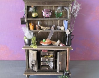 Może przedstawiać: Miniaturowa drewniana szafka z półkami i szufladami, ozdobiona w stylu Halloween. Zawiera pajęczyny, butelki z eliksirami, kociołek i miotłę.