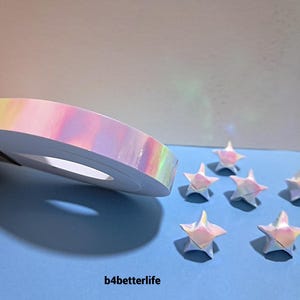 May include: A roll of iridescent tape and several origami stars are displayed on a blue surface. The tape has a rainbow sheen, and the stars are folded from similar paper. The text "b4betterlife" is visible.