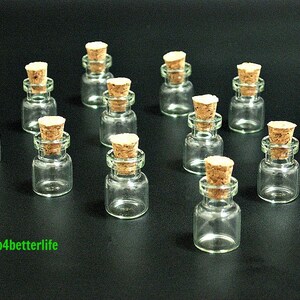 May include: A set of 12 small glass bottles with cork stoppers. The bottles are clear and the stoppers are brown. The bottles are arranged in a circle on a black background.