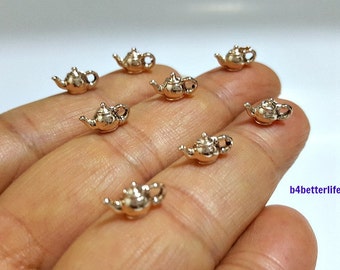 May include: Seven gold-colored miniature teapot charms. The charms are detailed with a spout, handle, and lid.
