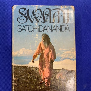 May include: A book cover with the title "Swami Satchidananda His Biography by Sita Wiener". The cover features a photo of a man in a pink robe walking on a mountain path.