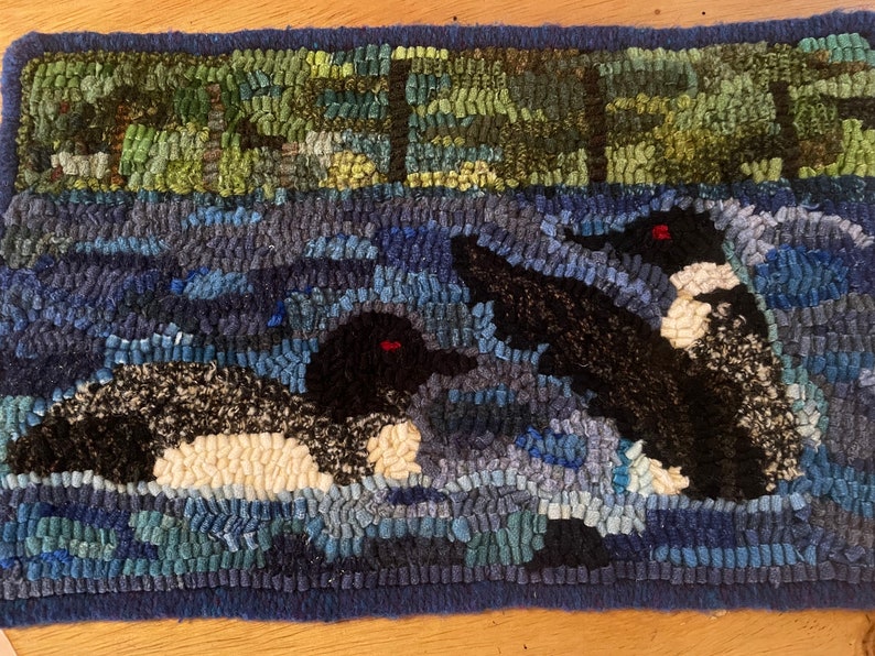 Hand hooked wool rug of two loons on a lake with trees in the background