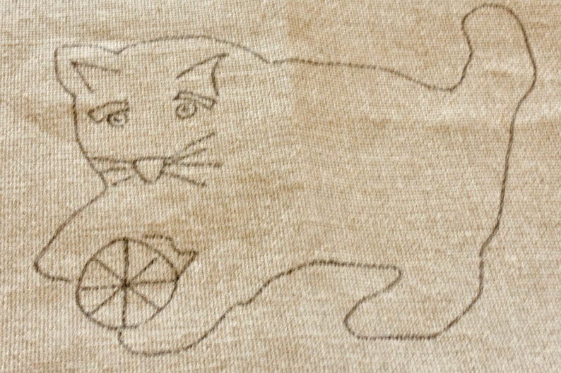 以下が含まれることがあります： ベージュの布地に描かれた、糸巻きで遊ぶ猫の手描きイラスト