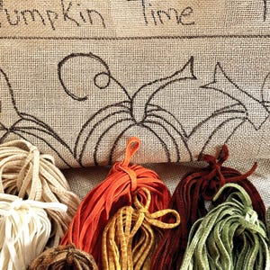 May include: A burlap bag with the words "Pumpkin Time" and a pumpkin design. Bundles of colorful shoelaces in shades of cream, orange, yellow, red, green, and brown are in front of the bag. The bag is approximately 18x9 inches.