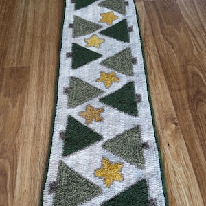 May include: A rectangular Christmas-themed rug with a white background. The rug features a repeating pattern of green Christmas trees and yellow stars. The trees alternate between dark and light green, and the stars are a golden yellow. The rug has a green border.