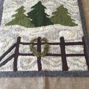 May include: A hand-hooked rug depicting a winter scene with three green trees, a brown fence, and a red and green wreath. The rug has a gray border and is set against a burlap background.