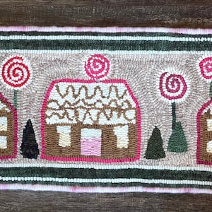 May include: Hand-hooked rug featuring three gingerbread houses with white icing, pink doors, and red and white swirl lollipops. The rug has a pink and green border and a light brown background.