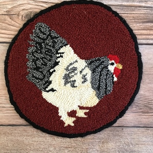 May include: A round, red and black rug with a white and black chicken design. The chicken is facing the right side of the rug.