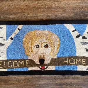 Hand hooked wool rug of a yellow Labrador holding a welcome home stick between two birch trees