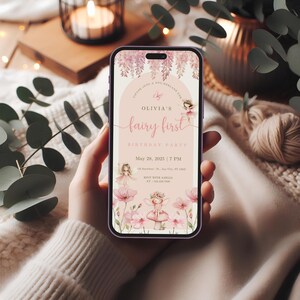 May include: A smartphone displays a pink and white invitation for "Olivia's Fairy First Birthday Party." The design features floral and fairy illustrations, with text including the date, time, and RSVP information. The phone is held in a hand.