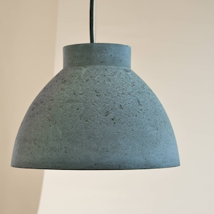 Op de afbeelding: Een grijze betonnen hanglamp met een afgeronde koepelvorm.