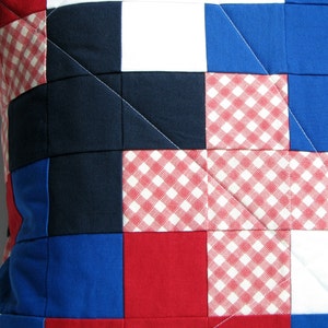 May include: A patchwork pillow cover with a red, white, and blue color scheme. The fabric is a mix of solid colors and gingham patterns.