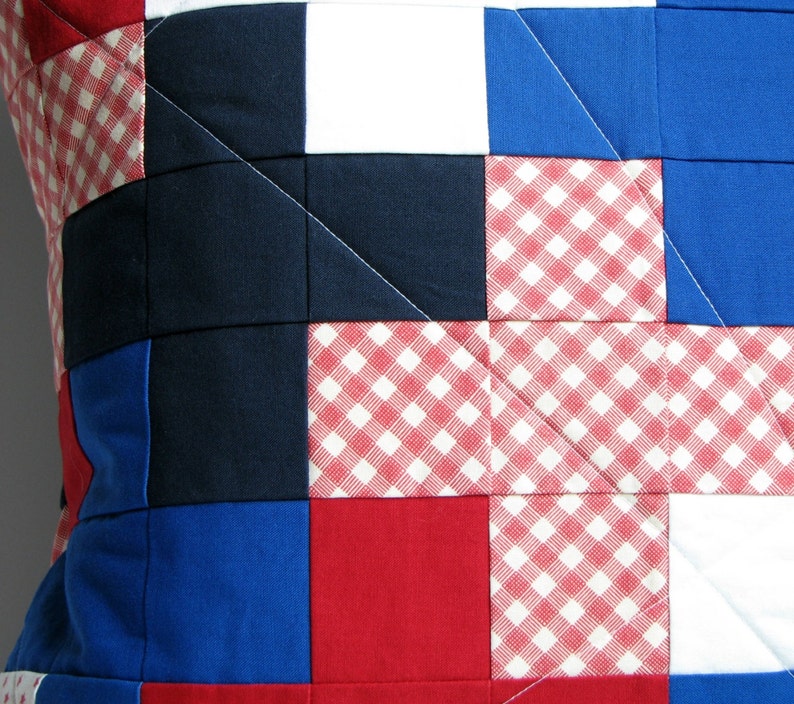 May include: A patchwork pillow cover with a red, white, and blue color scheme. The fabric is a mix of solid colors and gingham patterns.