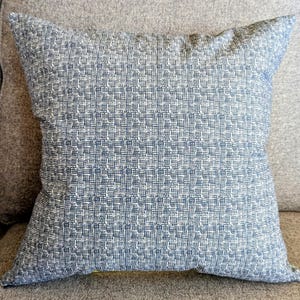 May include: A blue and white patterned throw pillow with a subtle geometric design. The pillow is made of a soft, textured fabric.