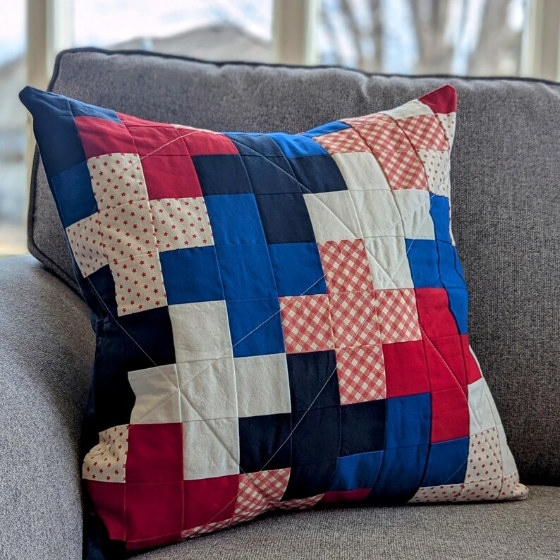 May include: A red, white, and blue patchwork pillow with a geometric design. The pillow is made of different fabrics, including gingham and polka dots.