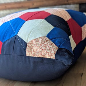 May include: A patchwork pillow with a geometric design in red, white, and blue fabrics. The pillow is made of different fabrics and has a navy blue border.