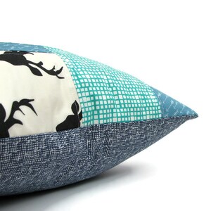 May include: A blue and white patchwork pillow with a deer silhouette design. The pillow is made of different fabrics with a variety of patterns, including a grid pattern and a small arrow pattern.