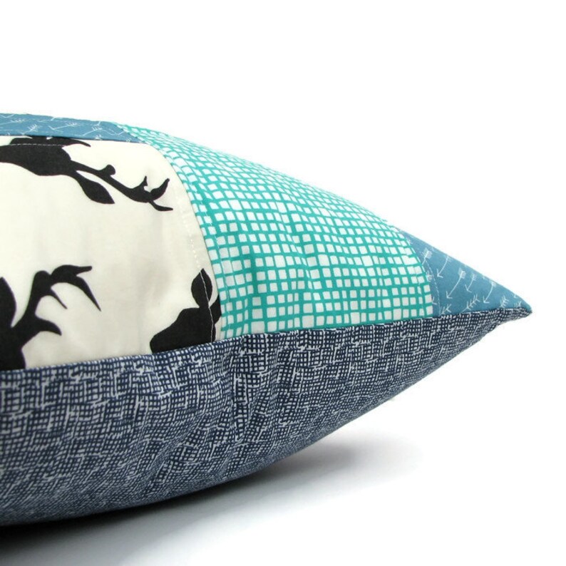 May include: A blue and white patchwork pillow with a deer silhouette design. The pillow is made of different fabrics with a variety of patterns, including a grid pattern and a small arrow pattern.