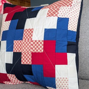 May include: A red, white, and blue patchwork pillow with a gingham pattern. The pillow is made of different fabrics and has a geometric design.
