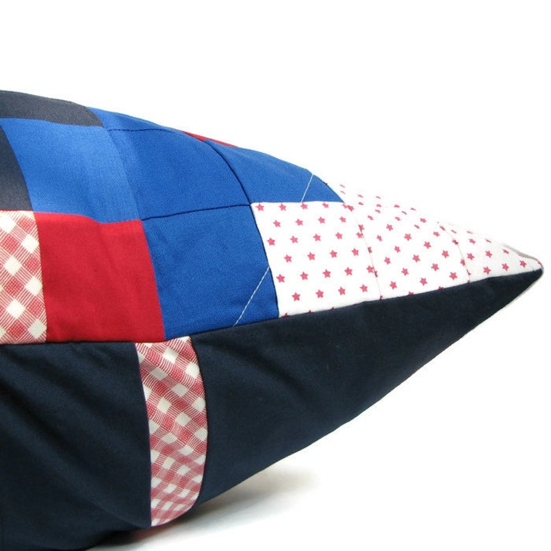 May include: A patchwork pillow with red, white, and blue squares and a gingham pattern. The pillow is made of fabric and has a pointed end.