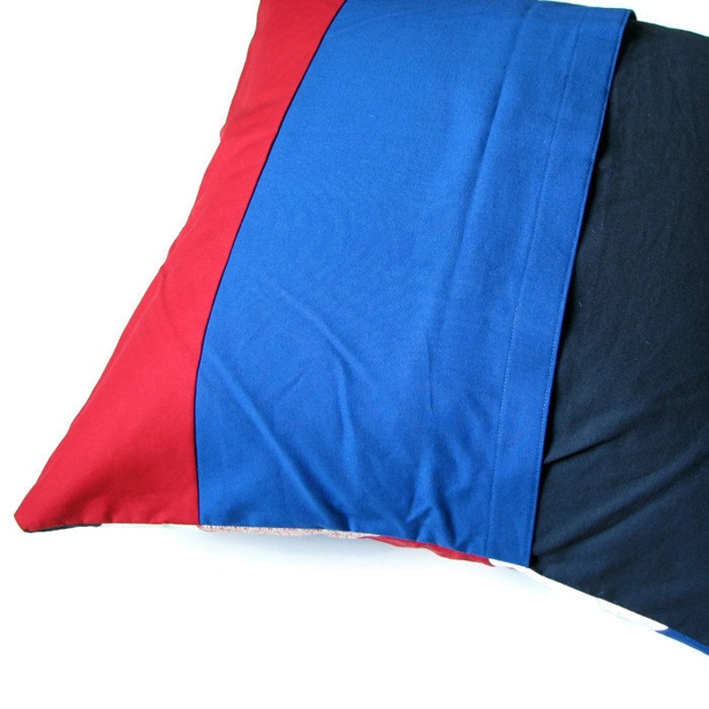 May include: A red, blue and black pillow with a striped pattern. The pillow is made of a soft, textured fabric.