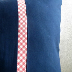 May include: A navy blue pillow with a red and white gingham trim down the center.