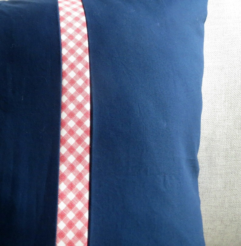 May include: A navy blue pillow with a red and white gingham trim down the center.