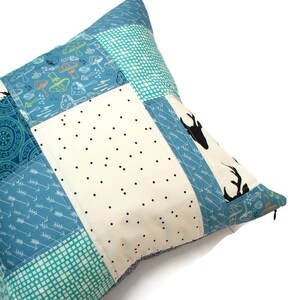 May include: A patchwork pillow with a zipper closure. The pillow is made of different fabrics with various patterns, including mushrooms, arrows, and polka dots. The pillow is in shades of blue, white, and green.