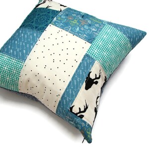 May include: A patchwork pillow with a cream background and blue, green, and black patterned fabric. The pillow features a deer silhouette design.