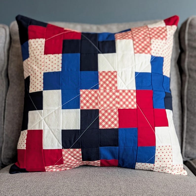 May include: A red, white, and blue patchwork pillow with a geometric design. The pillow is made of different fabrics with various patterns, including gingham and polka dots.