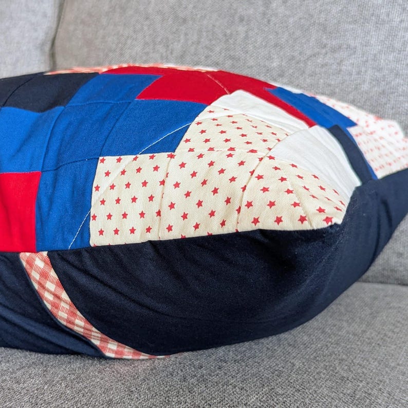 May include: A red, white, and blue patchwork pillow with a star pattern. The pillow is made of different fabrics and has a gingham pattern on the bottom.