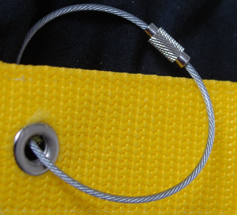 May include: Close-up of a silver metal cable loop with a textured clasp, attached to a yellow fabric with a metal grommet. The background is black. The cable is approximately 6 inches in diameter.