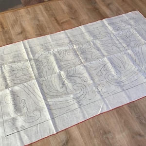 May include: A rectangular, off-white fabric with a red border, featuring a detailed black line drawing of floral and leaf patterns. The text "VINTAGE PATTERN BY LITHA" is visible at the top. The fabric is laid out on a wooden surface.