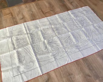 May include: A rectangular, off-white fabric with a red border, featuring a detailed black line drawing of floral and leaf patterns. The text "VINTAGE PATTERN BY LITHA" is visible at the top. The fabric is laid out on a wooden surface.