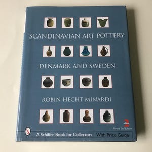 May include: A book titled "Scandinavian Art Pottery Denmark and Sweden" by Robin Hecht Minardi. The cover is a muted blue with images of pottery and text. The book is a Schiffer Book for Collectors.