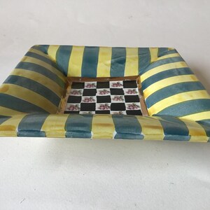 May include: Square decorative dish with a yellow and teal striped border. The center of the dish features a checkerboard pattern with pink floral accents. The dish has a slightly raised edge.