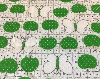 May include: White fabric with a repeating pattern of green apples with white polka dots and white butterflies with black outlines.