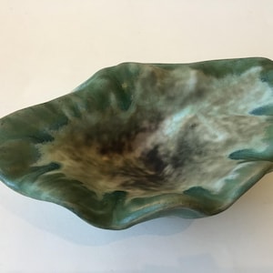 May include: A shallow, organic-shaped ceramic bowl with a wavy, ruffled rim. The glaze features a blend of deep forest green along the edges, transitioning into a soft, creamy white and dark brown mottled center with a smooth, glossy finish.