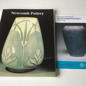 May include: Two books on Newcomb Pottery. The larger book has a black cover with the title "Newcomb Pottery" and an image of a vase with a light green and blue design. The smaller book is titled "(FEMINIST) ORIGINS OF NEWCOMB POTTERY (1895-1940)".