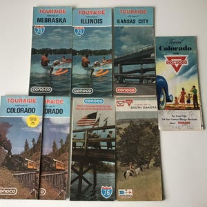 May include: A collection of vintage road maps from the "Touraide" series, featuring states like Nebraska, Illinois, and Colorado. The maps have colorful illustrations and the "Conoco" logo. One map promotes travel in Colorado.